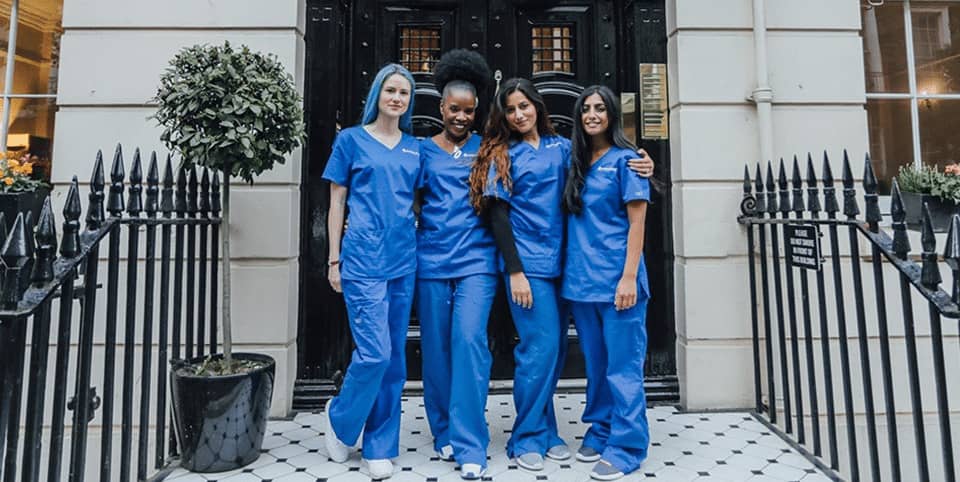 Four nurses in blue scrubs outside a Georgian clinic entrance for EMsculpt NEO body sculpting in Amsterdam